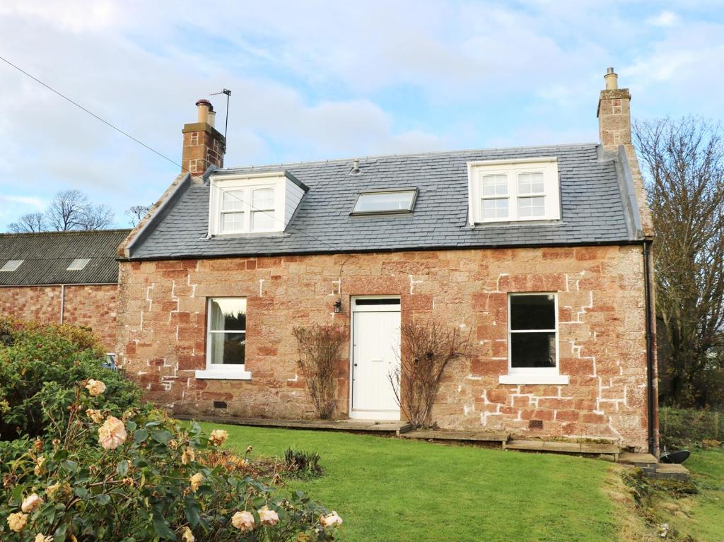 une maison en briques avec une porte blanche et une cour dans l'établissement The Grieves Cottage, à Haddington