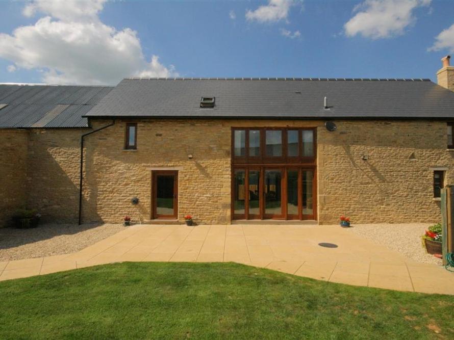 a brick building with glass doors and a courtyard at Tithe Barn, Lyneham in Bruern