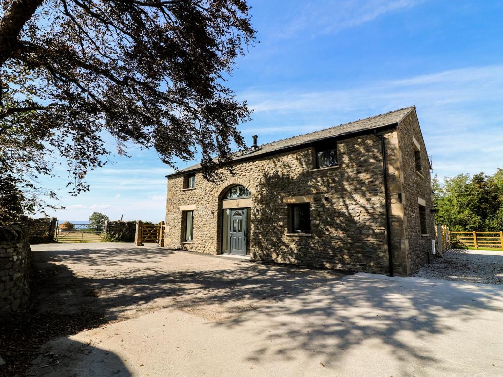 an old stone building with a tree in front of it at Damson Barn in Casterton