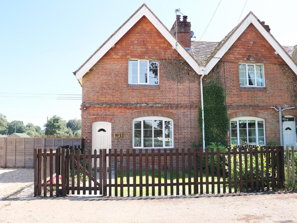 a brick house with a wooden fence in front of it at New Park Farm Cottage in Brockenhurst
