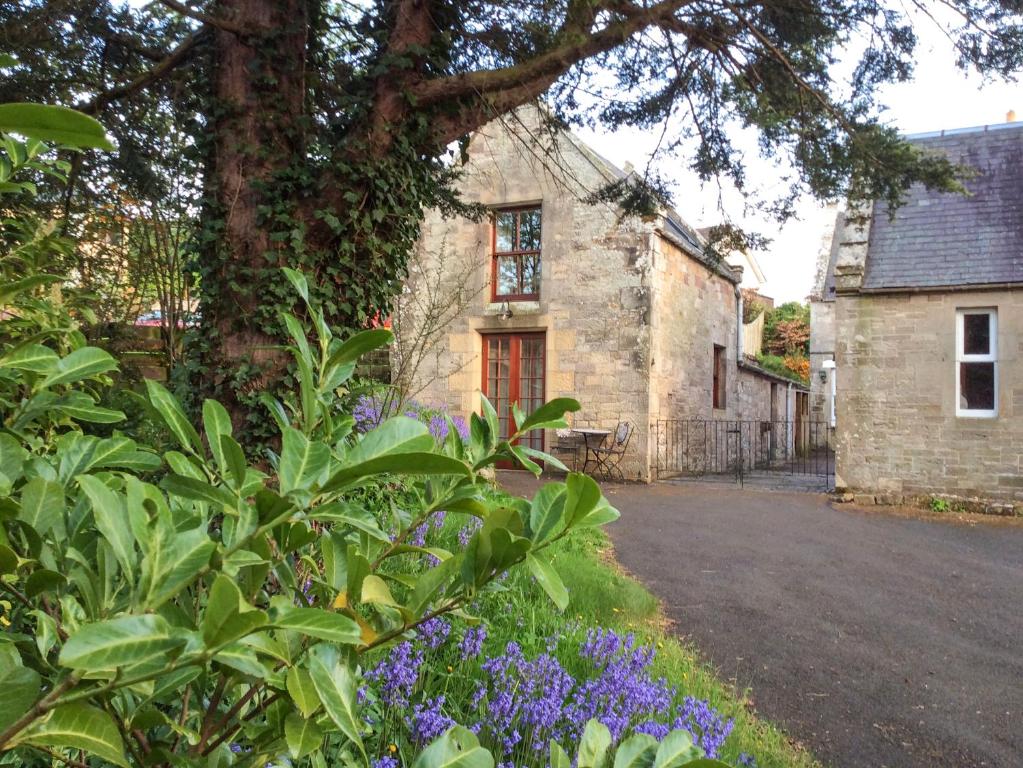 an old stone house with purple flowers in front of it at Allerton House Stables in Jedburgh