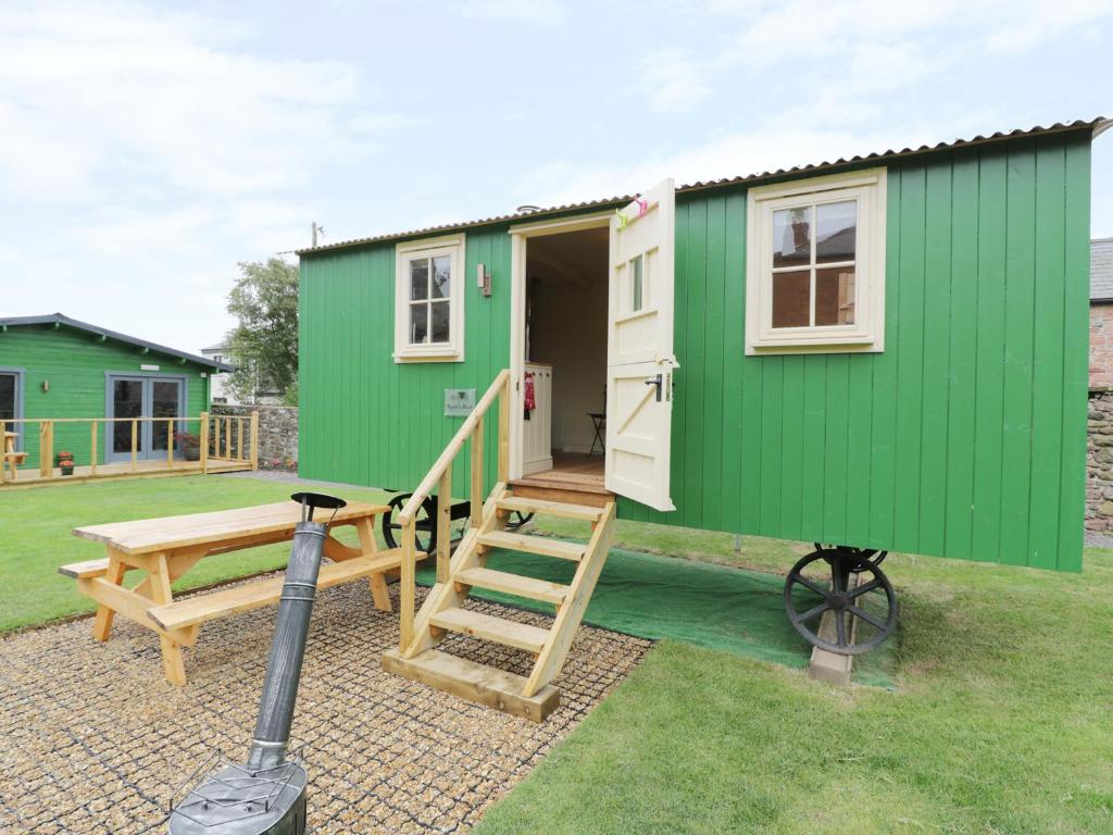 a green tiny house with a table and a bench at Ryan's Rest in Bowness-on-Solway