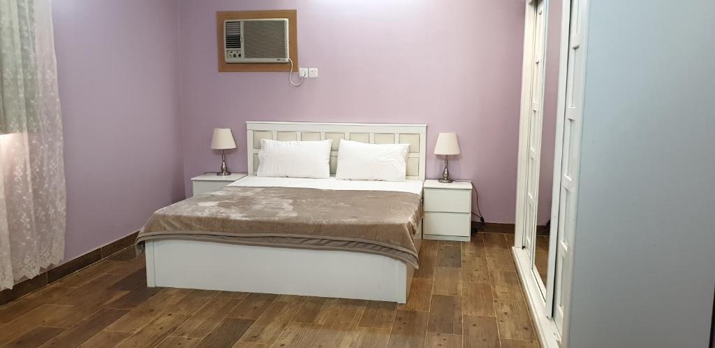 a bedroom with a white bed and two night stands at استراحة البيت الريفي in Umm Lujj
