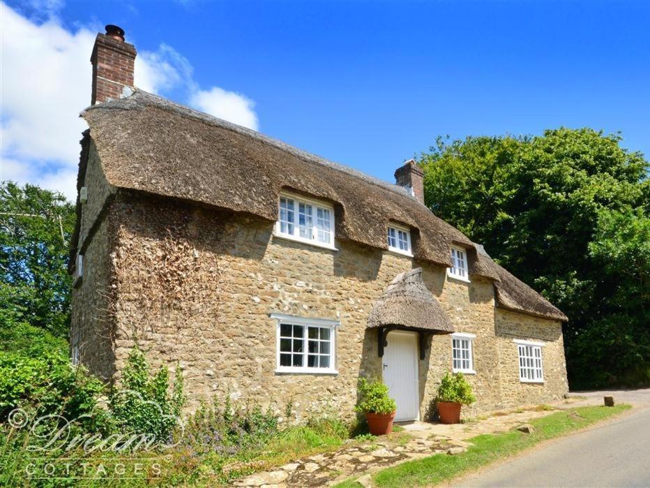 an old stone house with a thatched roof at Little Berwick Cottage in Burton Bradstock