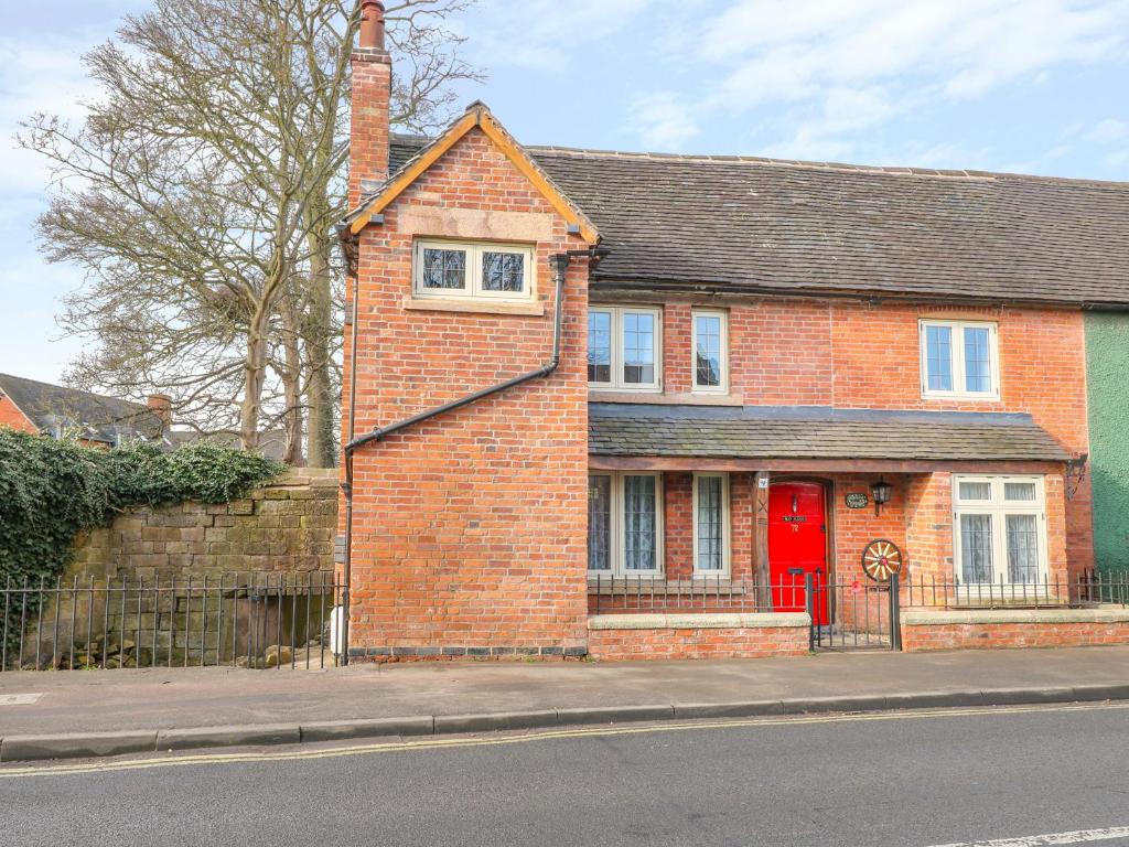 a brick house with a red door on a street at Jasmine Cottage in Belper