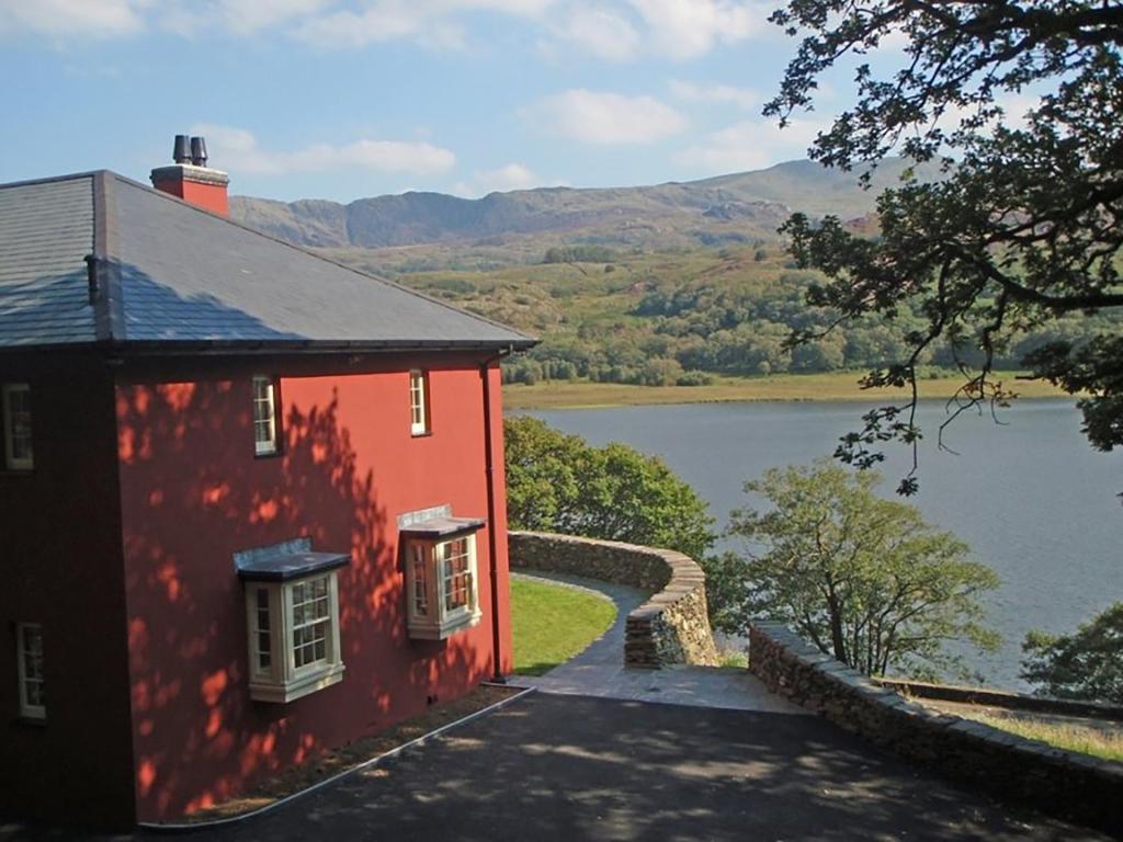 a red house next to a body of water at Dinas Noddfa in Beddgelert