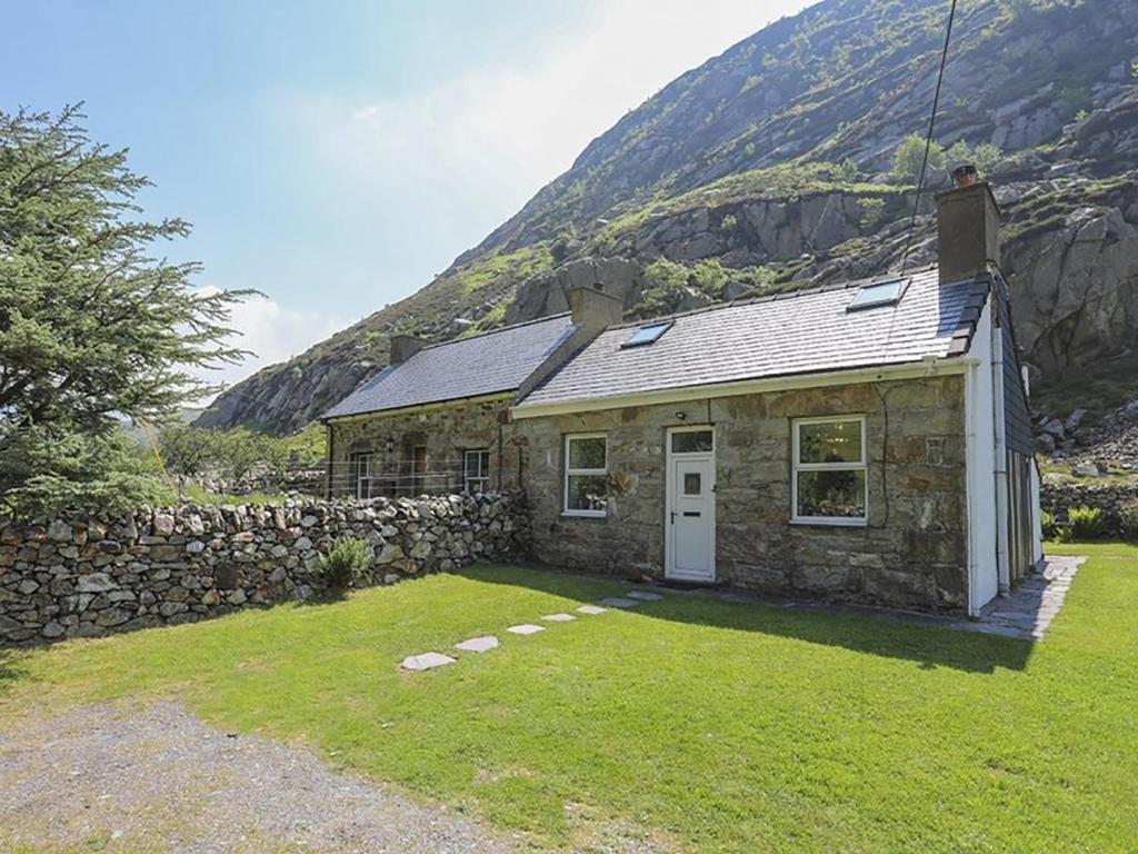 a stone house in front of a stone wall at Tan Meredydd in Nantlle