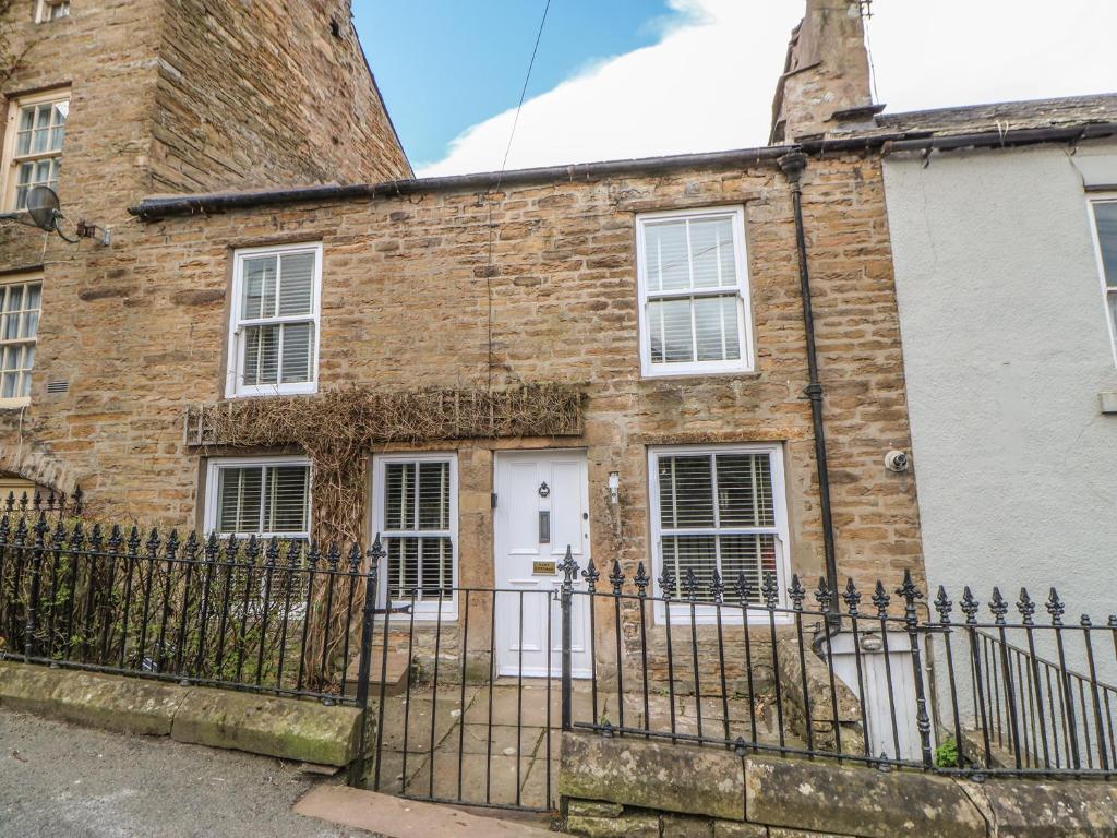 een oud stenen huis met een ijzeren hek bij Bank Cottage in Alston