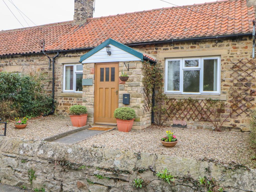 a stone house with a brown door and potted plants at Rose Cottage in Darlington