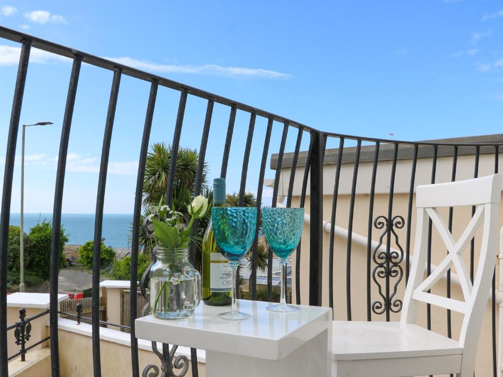 a table with two blue glasses and flowers on a balcony at 10 Cove View in Ilfracombe