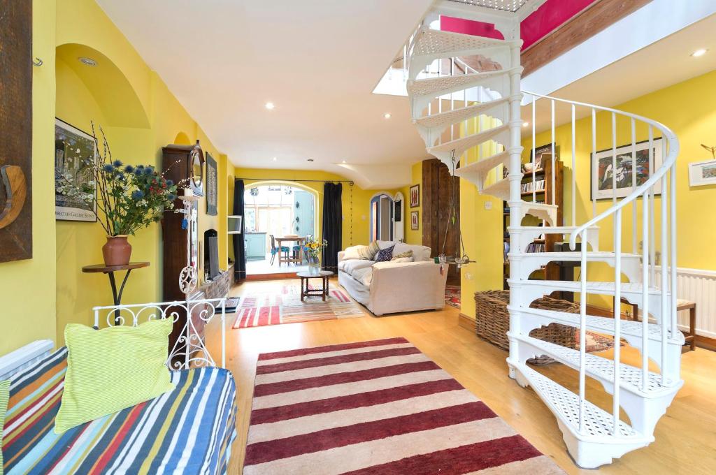 a living room with yellow walls and a white spiral staircase at Veeve - Boho Charm in London