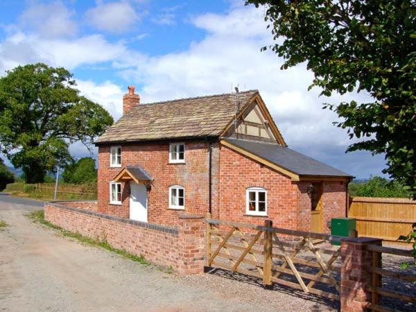 a small brick building with a wooden fence at Point Cottage in Blakemere