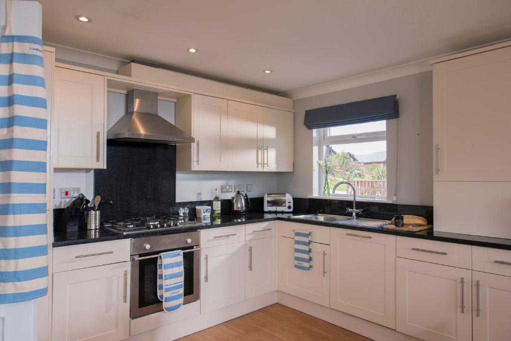 a kitchen with white cabinets and a sink and a window at Padstow 2 bedroom Lodge at Retallack Resort in Padstow