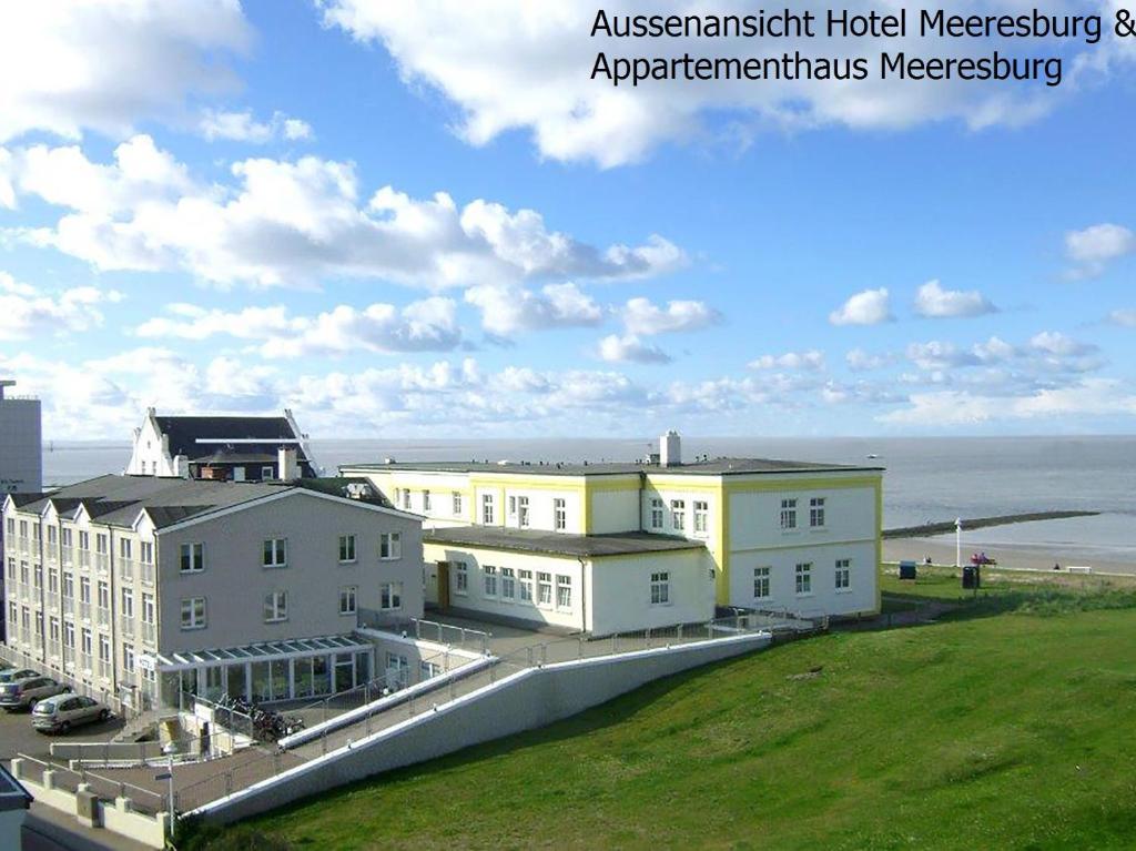 Hotel Meeresburg في نورديرني: مجموعة من المباني مع المحيط في الخلفية
