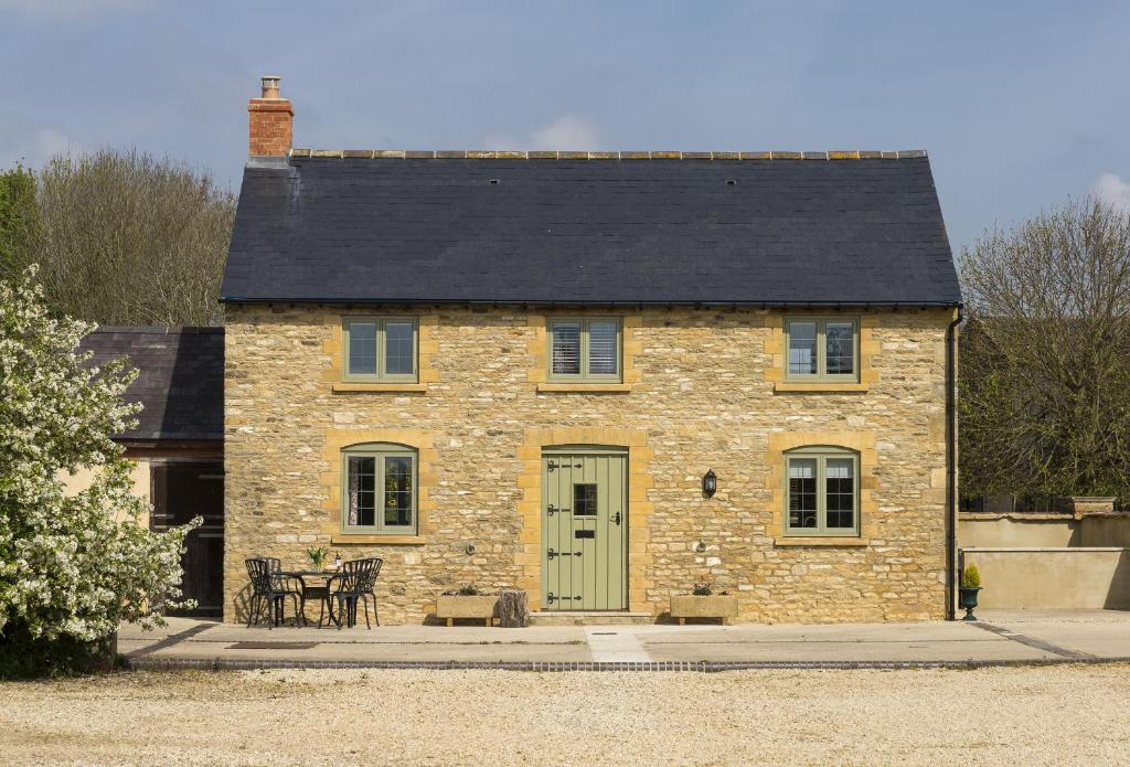 a stone house with a black roof and a green door at Alysas Cottage in Chipping Norton