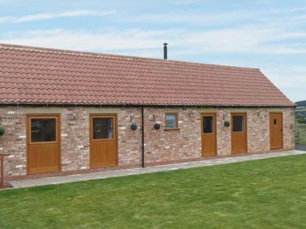 a brick building with brown doors and a grass field at Pottowe Cottage in Potto