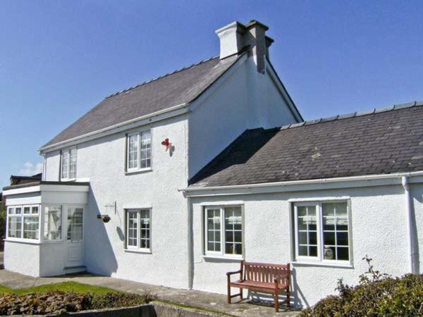 ein weißes Haus mit einer Bank davor in der Unterkunft Tyddyn Gyrfa Cottage in Cemaes Bay