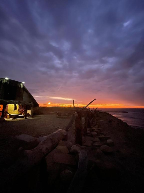 a building on the beach with the sunset in the background at La Casa del Naufrago in Lobitos