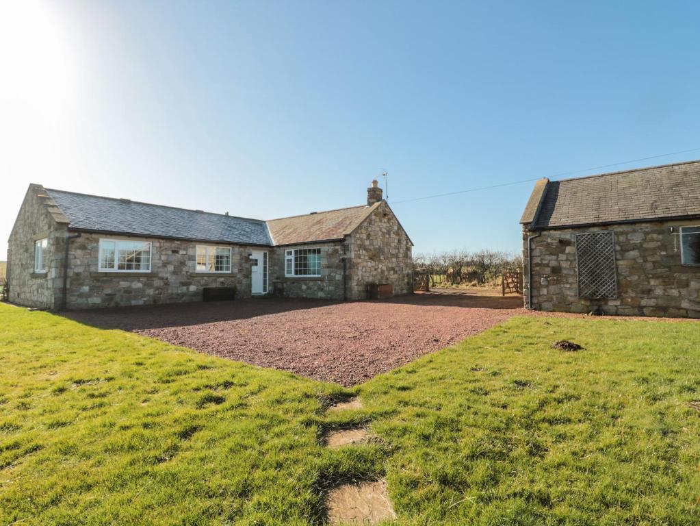 an old stone house with a grassy field in front of it at Thistleyhaugh Cottage in Morpeth