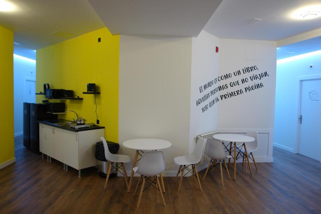 a room with three tables and a kitchen with yellow walls at Hostel Trovadores in Burgos