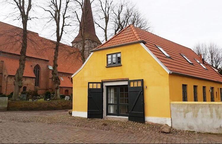 a yellow building with a red roof on a street at Historisches Pastorat - Villa Mika in Fehmarn