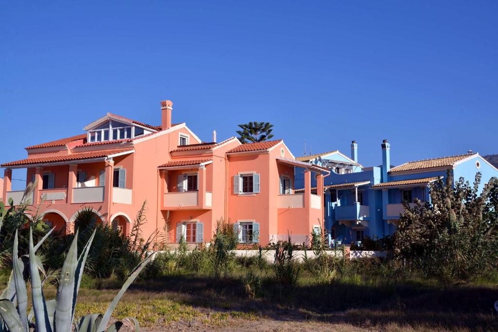 a large pink house on the side of a beach at Vlachos Apartments Acharavi in Acharavi