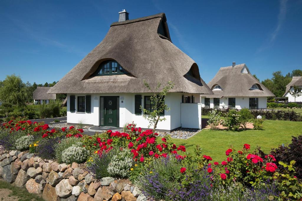 dwa kryte strzechą domki z kwiatami w ogrodzie w obiekcie Ferienhaus Seeadler 34 w mieście Fuhlendorf