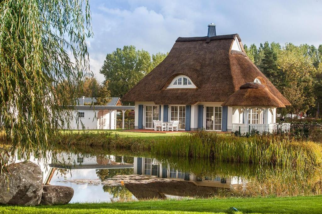 a thatched cottage with a pond in front of it at Ferienhaus Haubenlerche 20 in Fuhlendorf