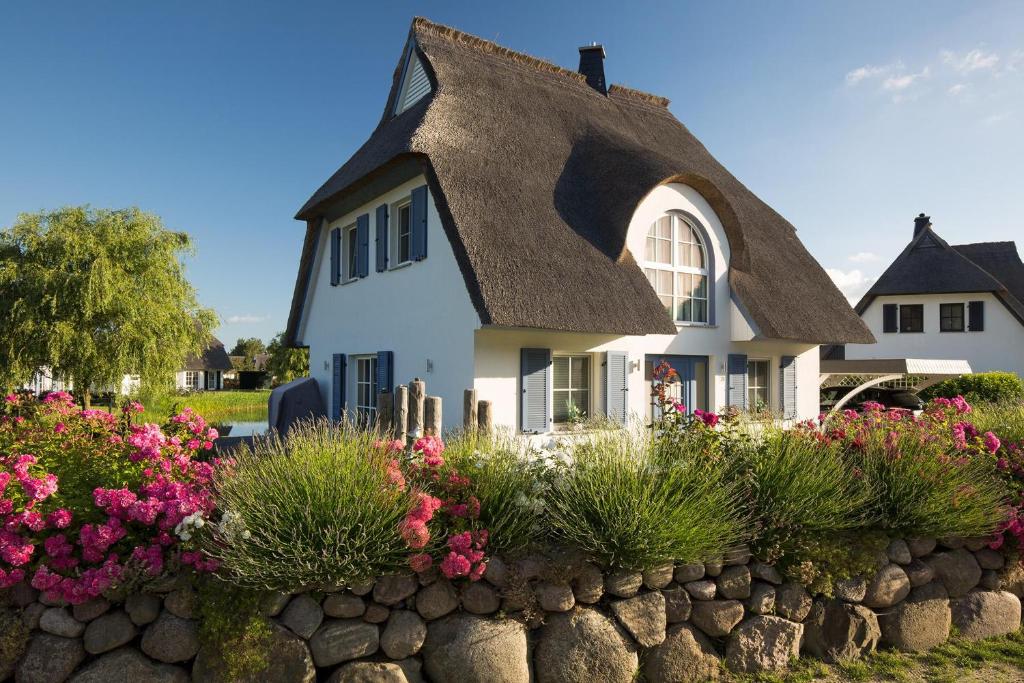 ein weißes Haus mit einem Strohdach und Blumen in der Unterkunft Ferienhaus Schilfrohrsaenger 18 in Fuhlendorf