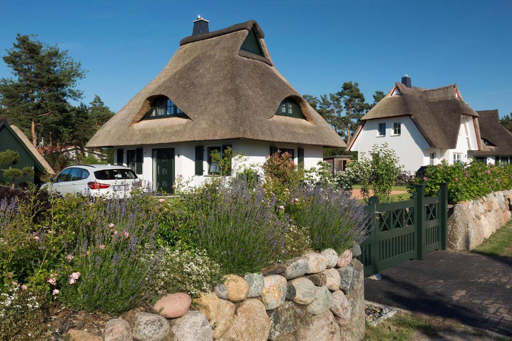 a thatched house with a retaining wall and flowers at Ferienhaus Seeadler 9 in Fuhlendorf