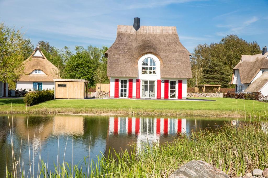 a house with a thatched roof reflected in a pond at Ferienhaus Schilfrohrsaenger 26 in Fuhlendorf