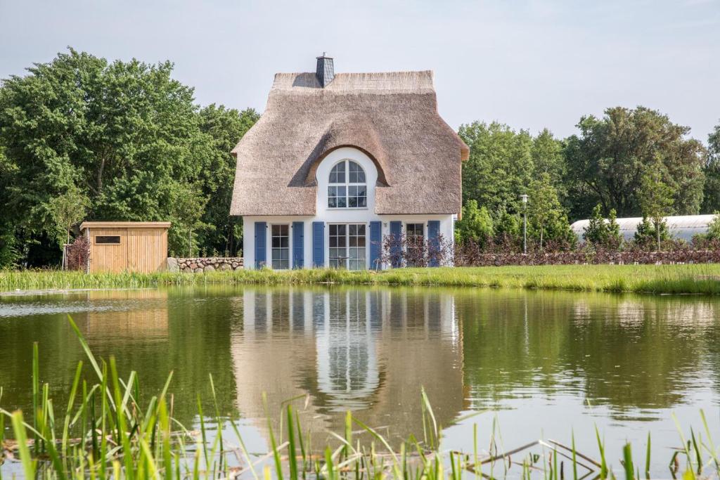 a house with a thatched roof reflected in a pond at Ferienhaus Schilfrohrsaenger 28 in Fuhlendorf
