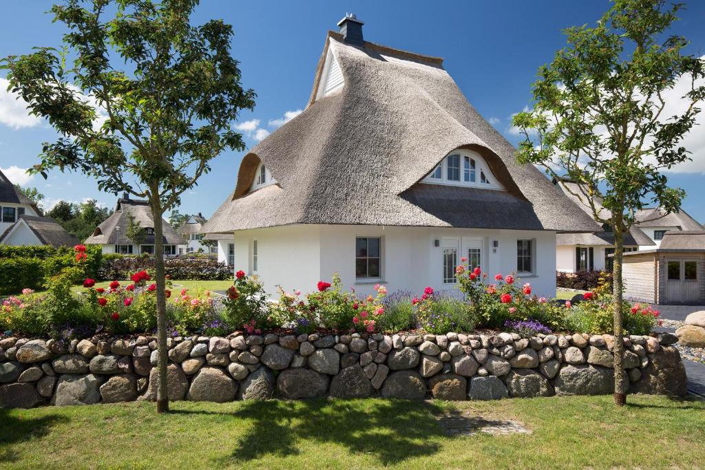 a thatched house with a retaining wall and flowers at Ferienhaus Seeadler 24 in Fuhlendorf