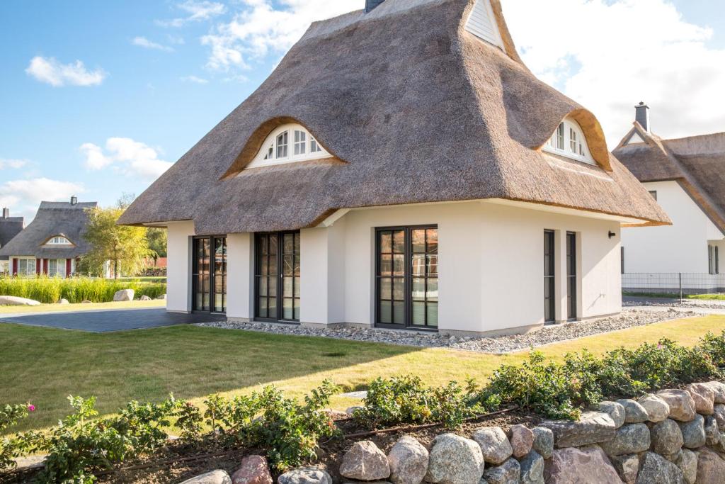 a thatched roof house with a stone wall at Ferienhaus Haubenlerche 32 in Fuhlendorf