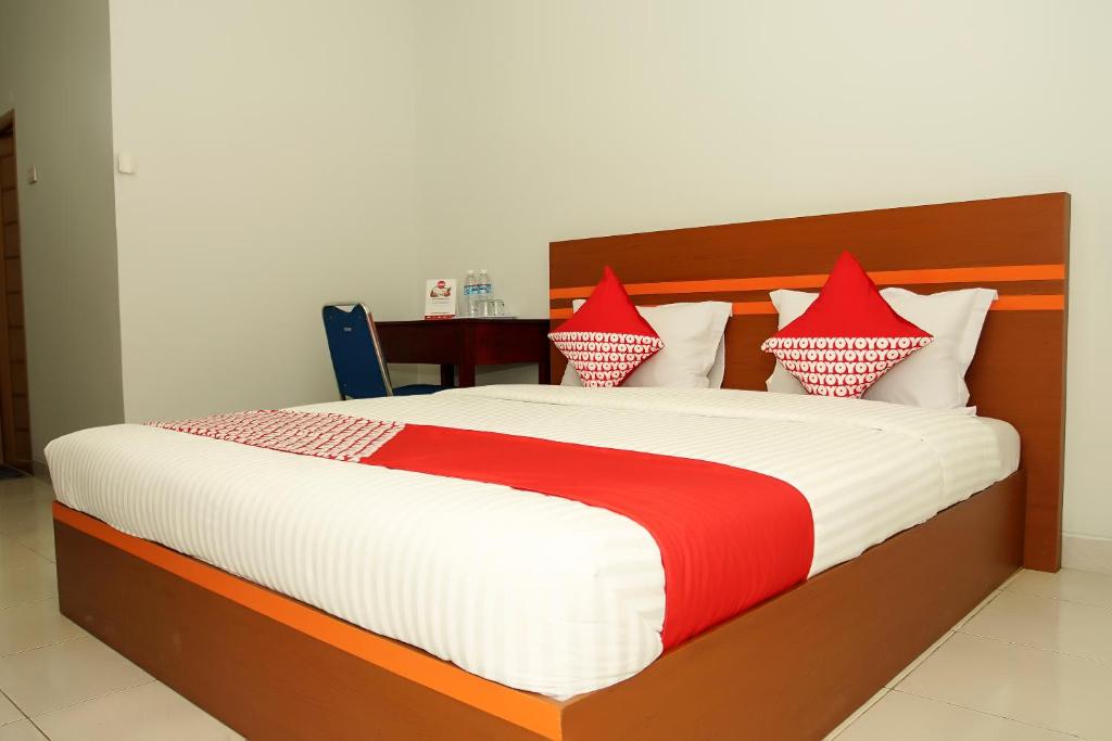 uma cama com lençóis e almofadas vermelhos e brancos em OYO Life 189 AA Residence Syariah em Sukarami