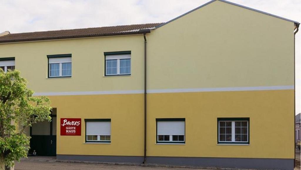 ein gelbes und weißes Gebäude mit einem roten Schild darauf in der Unterkunft BAUERs Gästehaus in Obersiebenbrunn