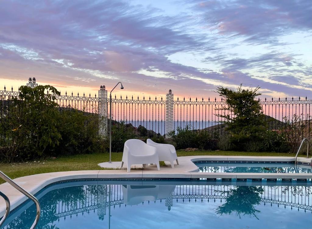 una piscina con due sedie bianche e una recinzione di Alojamiento con Encanto en Málaga a Málaga