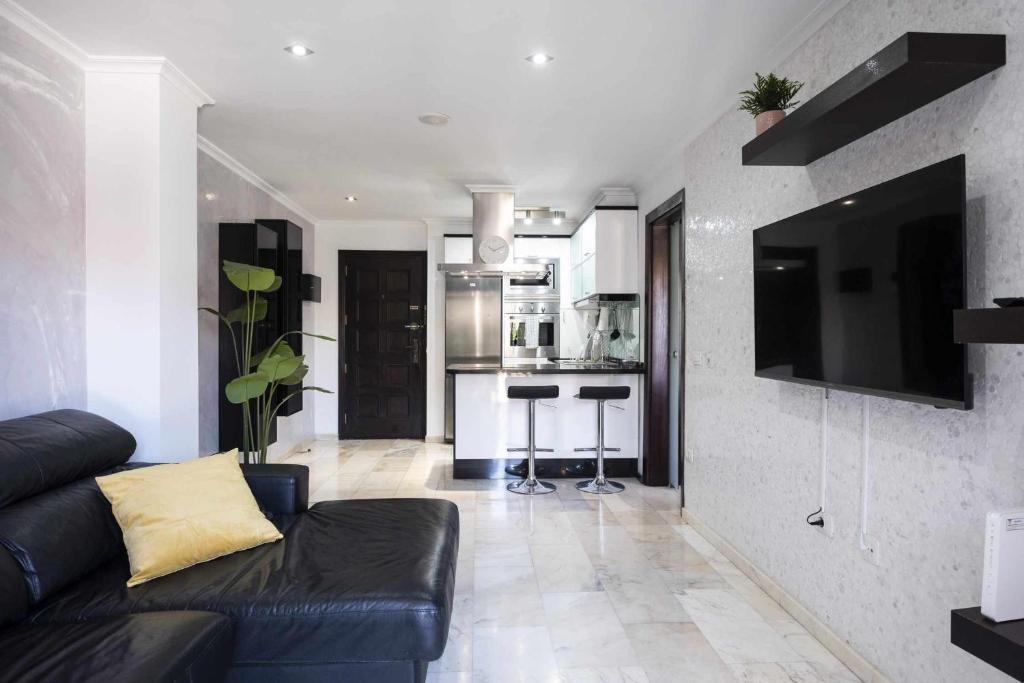 sala de estar con sofá negro y cocina en Renewed and Central Apartment, en Puerto de la Cruz