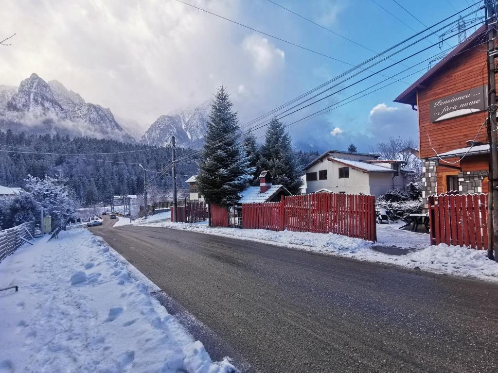 a snow covered street with a building and mountains at Pensiunea Fara Nume in Buşteni