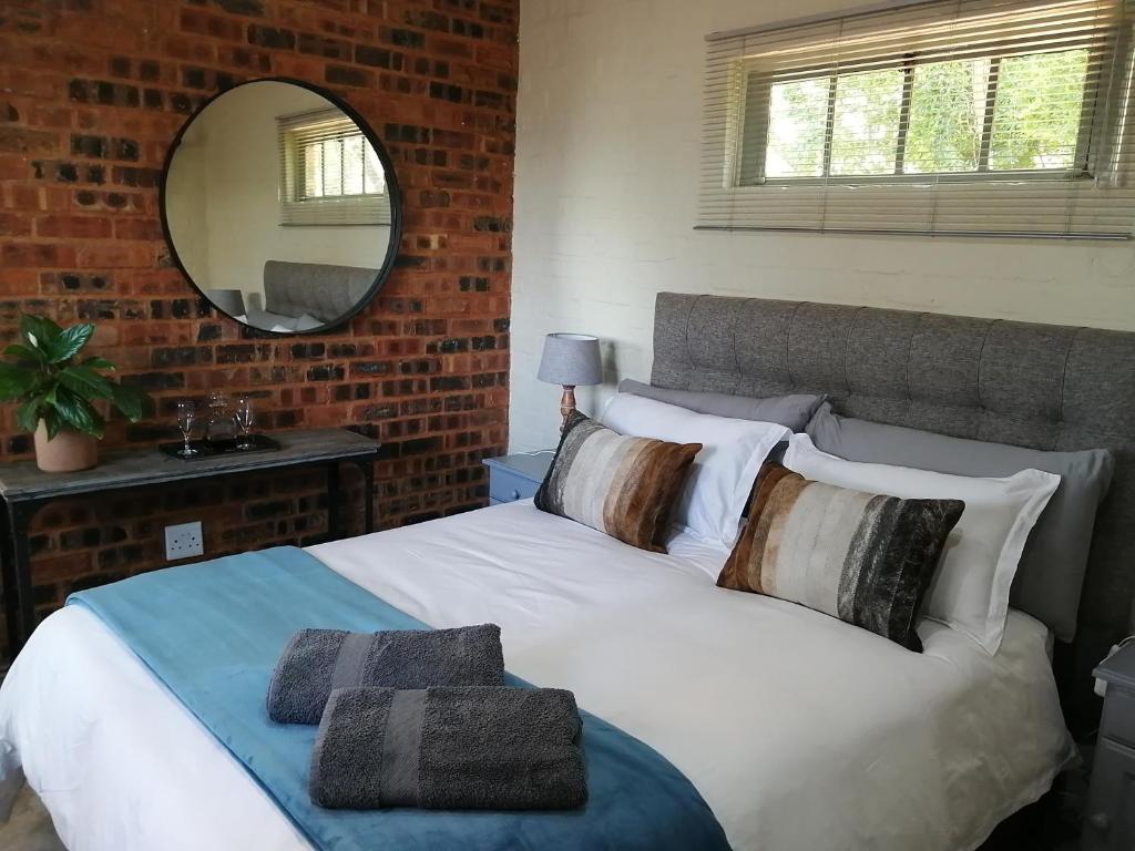 una camera da letto con letto bianco, cuscini e specchio di Bushbaby Cottage in Hartbeespoort a Pretoria
