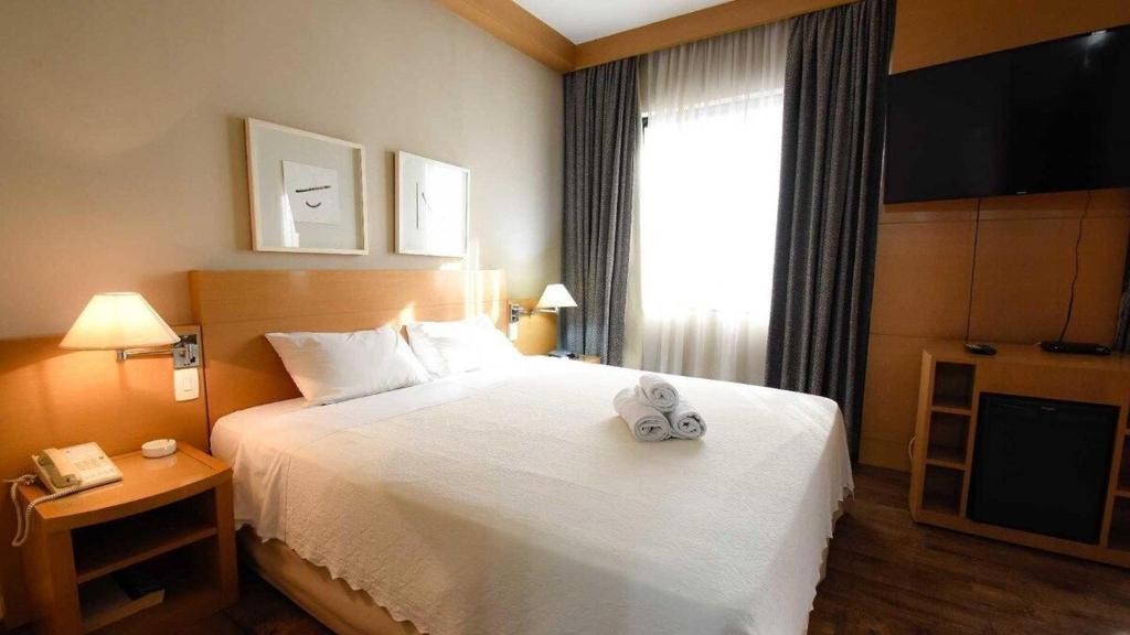 een hotelkamer met een wit bed en een televisie bij Flat 1208 Lazer completo - Prox. Shopping e Metrô in Sao Paulo