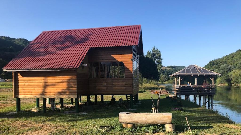 ein Holzhaus mit rotem Dach neben einem Fluss in der Unterkunft Vikendica Na Plivi in Šipovo