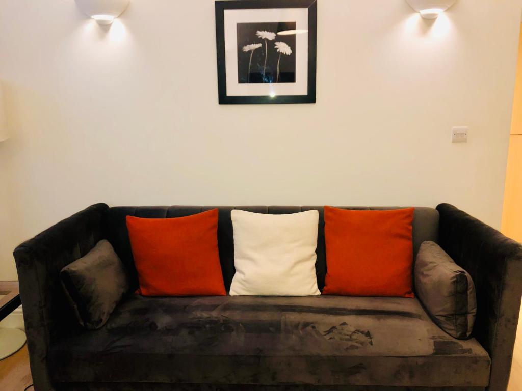 Luxury apartment in the heart of Bath في باث: أريكة بنية مع وسائد برتقالية وبيضاء عليها