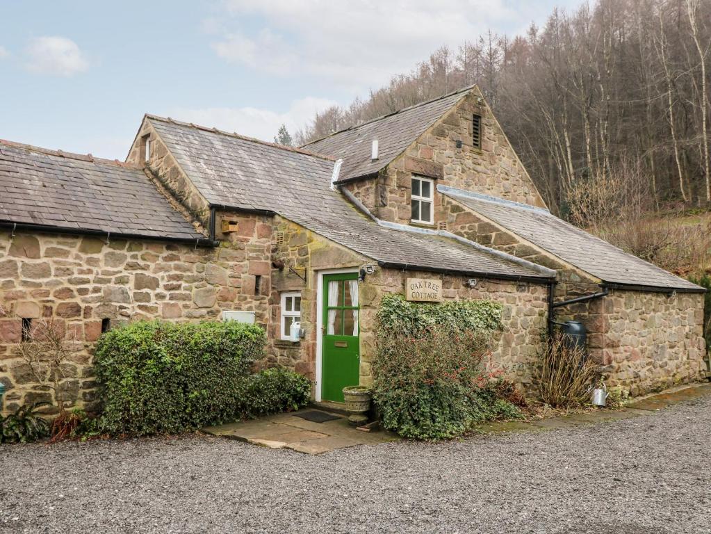 an old stone house with a green door at Oak Tree Cottage in Matlock