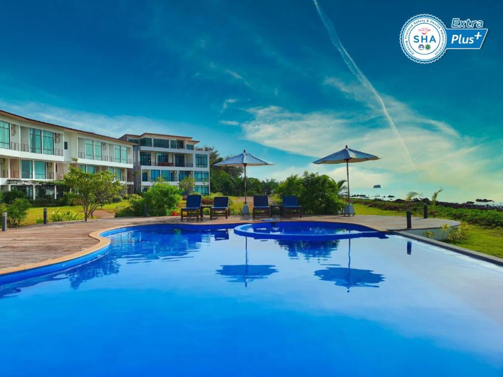 a large swimming pool at a resort with chairs and umbrellas at The Beach Resort & Residence - SHA Plus in Pathiu