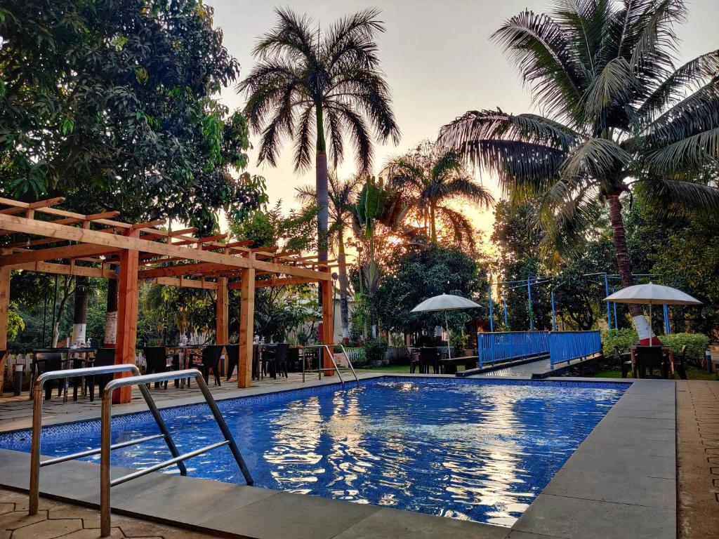 a swimming pool with palm trees in the background at Pushp Vatika Resort & Lawns in Navi Mumbai