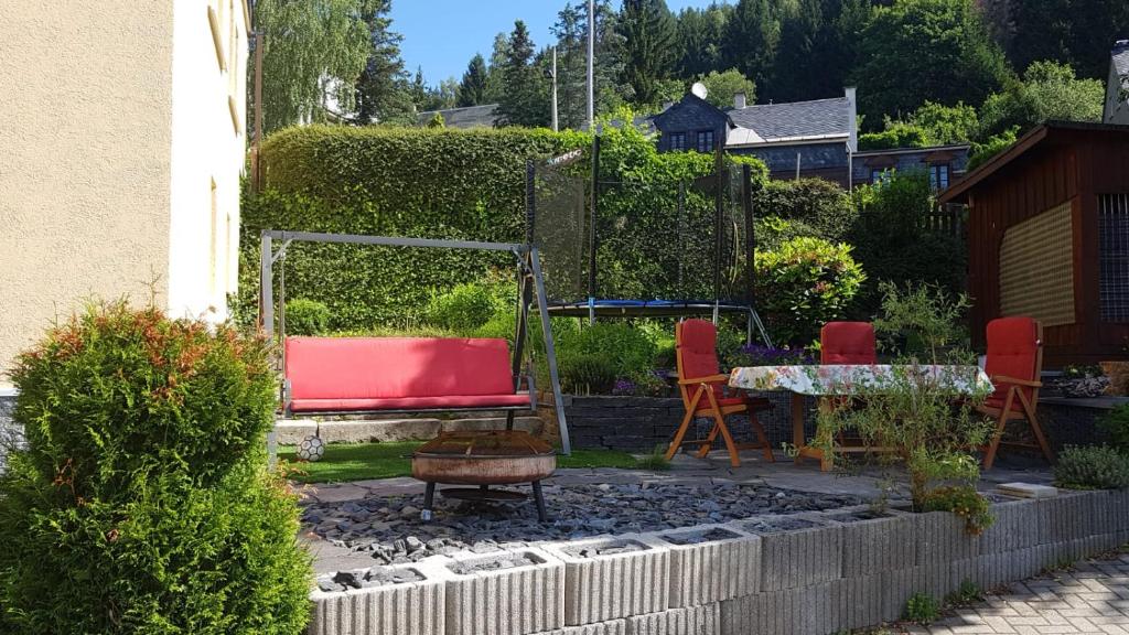 un jardín con sofá rojo, sillas y mesa en Ferienwohnung mit Garten und Spielplatz, en Klingenthal