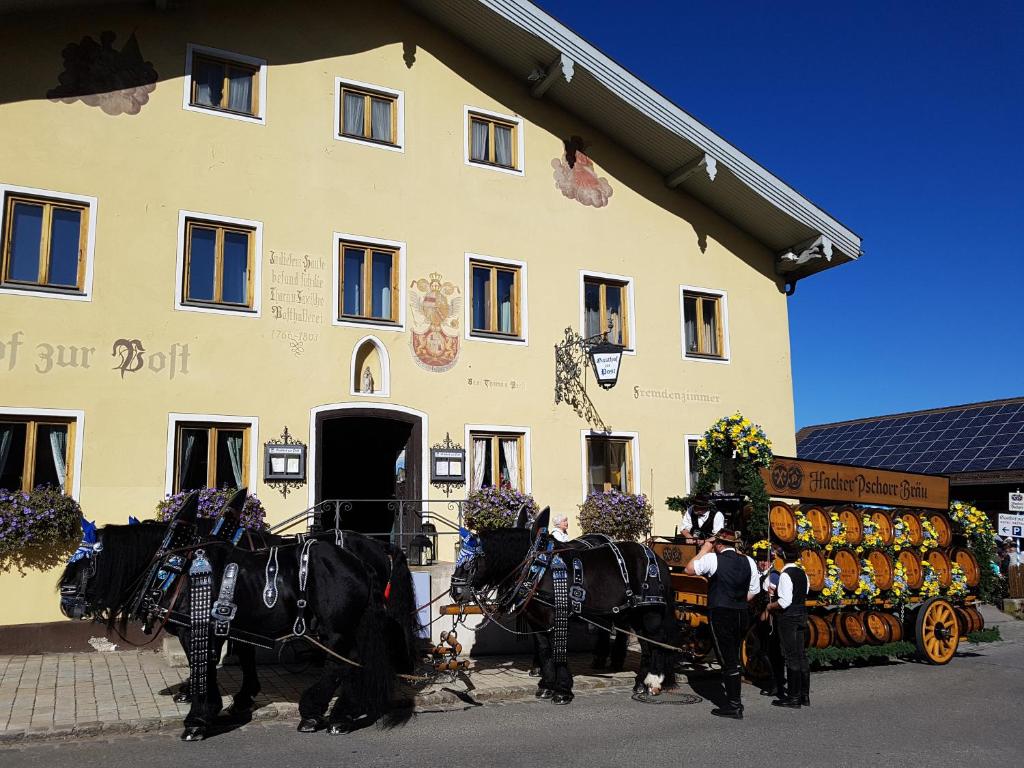 eine Gruppe von Pferden, die vor einem Gebäude einen Wagen ziehen in der Unterkunft Gasthof - Hotel zur Post in Pöcking