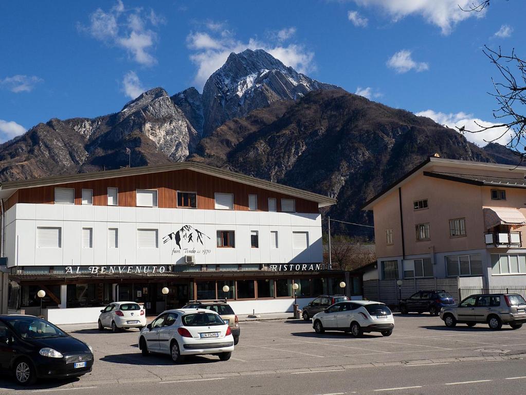 a building with cars parked in a parking lot with mountains at Al Benvenuto Hotel & Restaurant in Tolmezzo