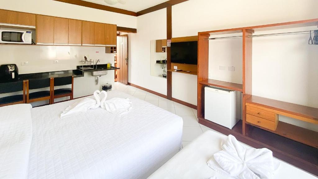 a bedroom with two white beds and a kitchen at Suítes Trilha do Sol in Ubatuba